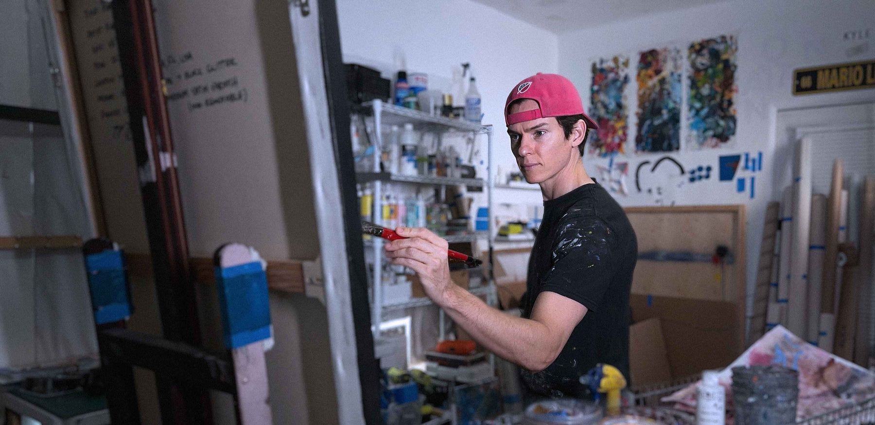 Portrait artist Kyle Lucks painting at his easel in his West Palm Beach studio, surrounded by colorful works in progress