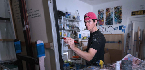 Portrait artist Kyle Lucks painting at his easel in his West Palm Beach studio, surrounded by colorful works in progress